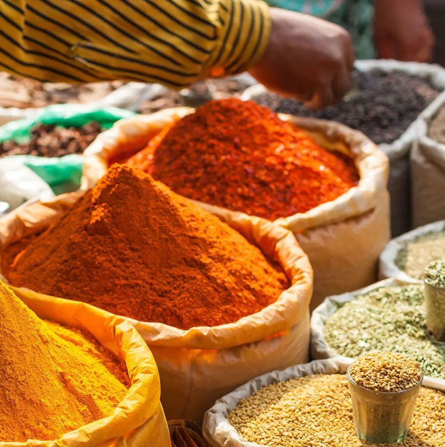 Bags of colorful spices at a market stall. A hand reaches into one.