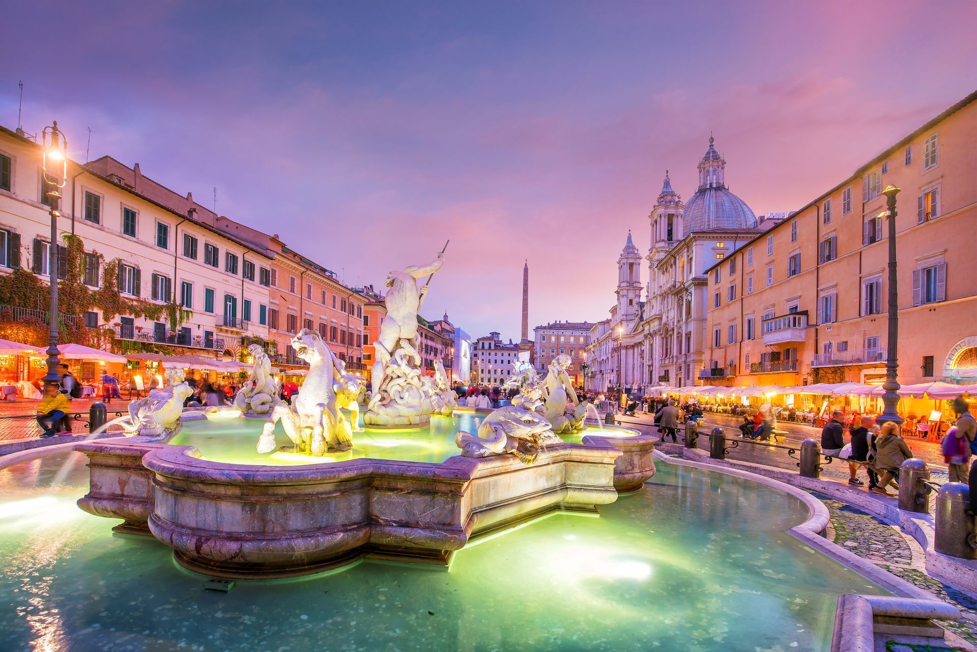 Fountain of Four Rivers in Piazza Navona, Rome. Illuminated figures, buildings, reflecting water, twilight sky.
