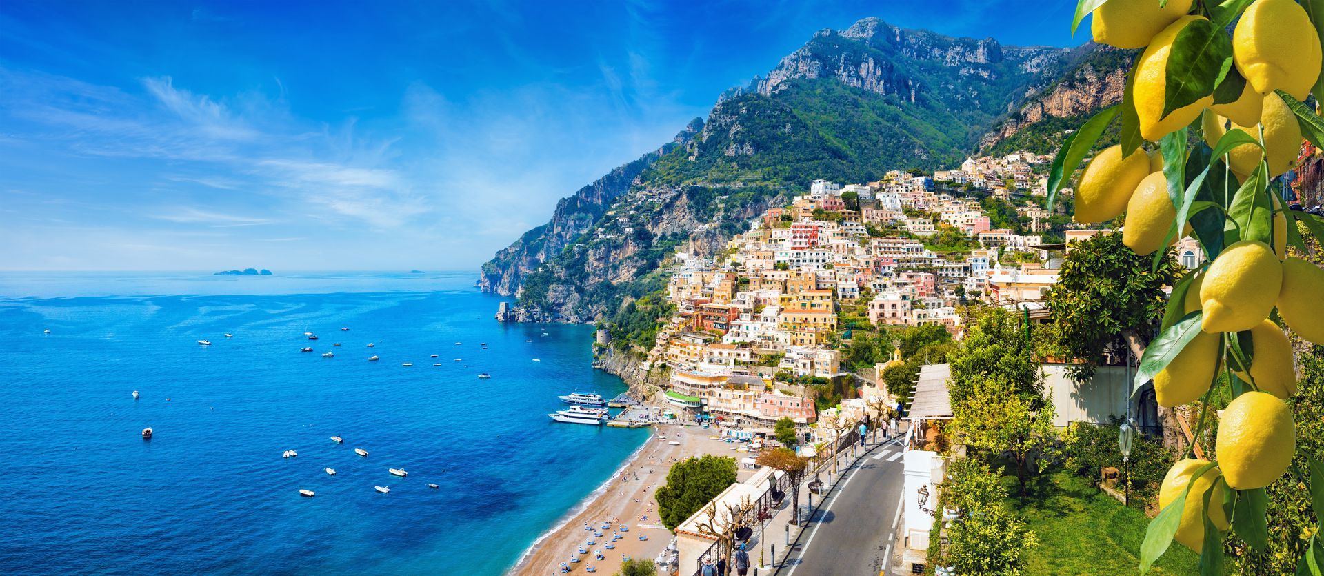 Coastal Italian village with lemons. Bright blue sea, mountains, colorful buildings, and a road along the shore.