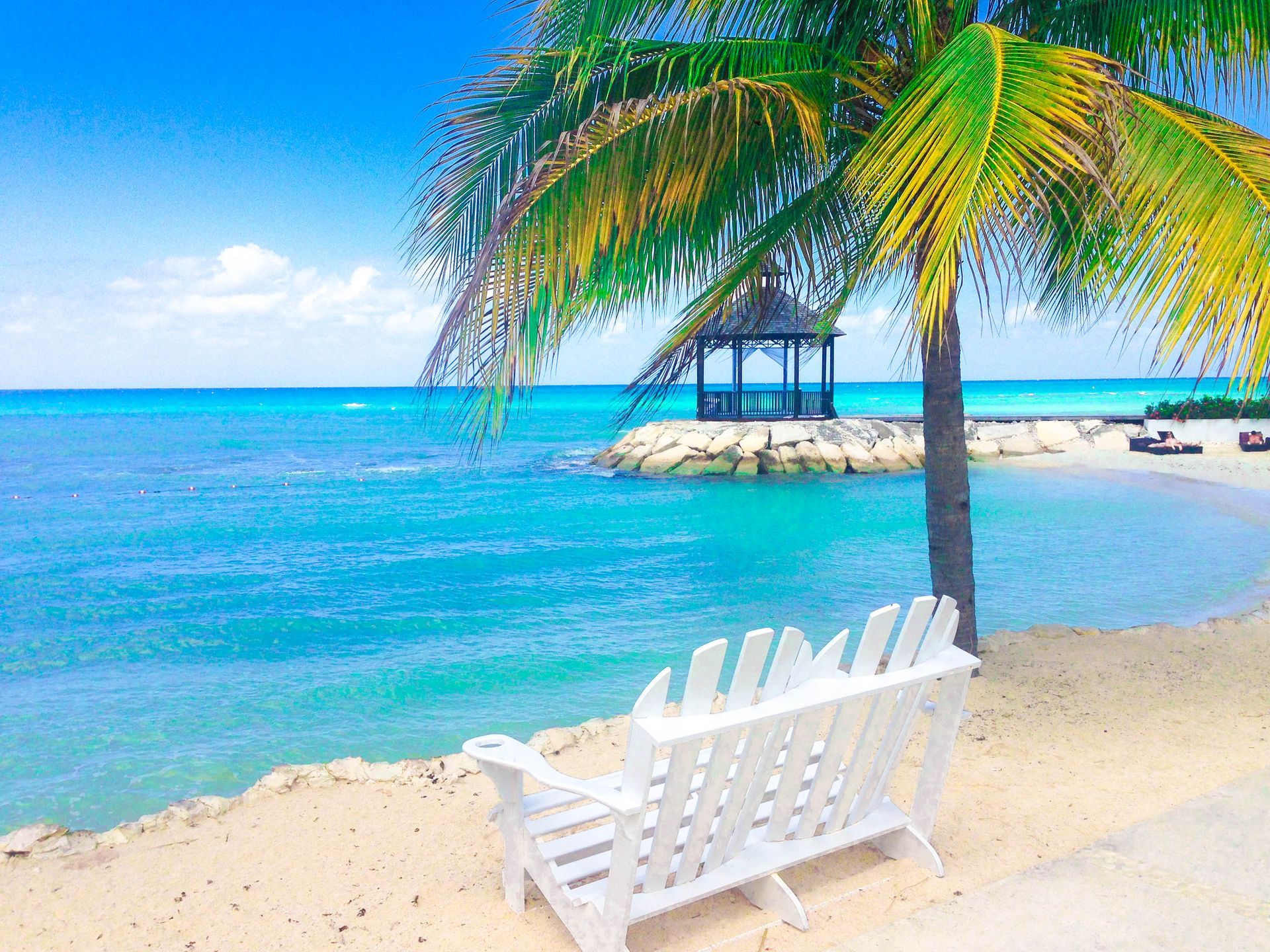 White Adirondack chairs on sandy beach facing turquoise ocean