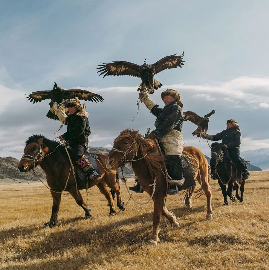 People on horseback in a field, each holding a large eagle with outstretched wings.