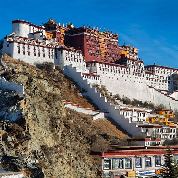 Potala Palace in Lhasa, Tibet, a large white and red complex on a hillside, against a bright blue sky.