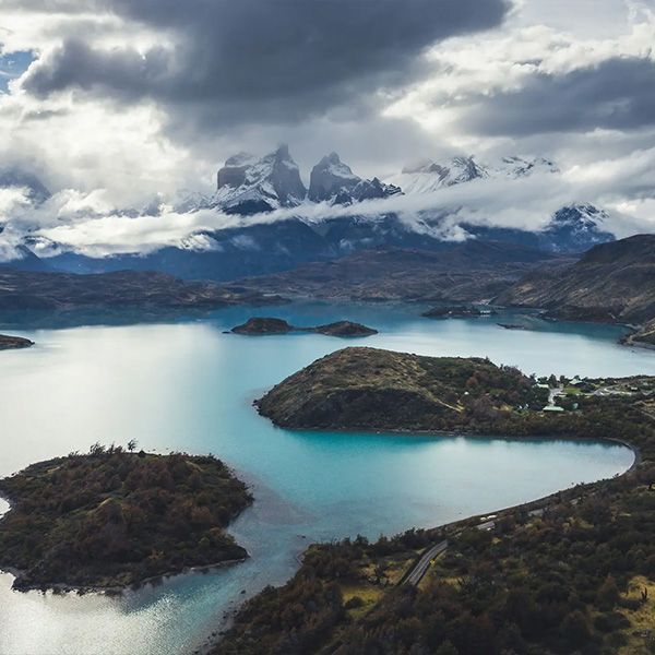 Lake and mountains in Torres del Paine National Park, Chile; turquoise water, dark islands, snow-capped peaks, and cloudy sky.