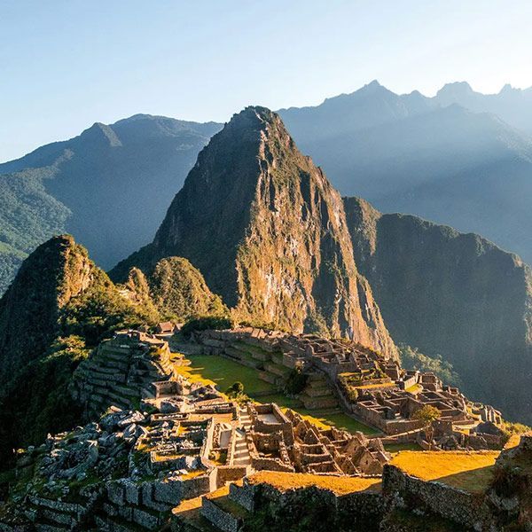Machu Picchu ruins in Peru, a stone city on a mountain peak with lush greenery, under sunlight.