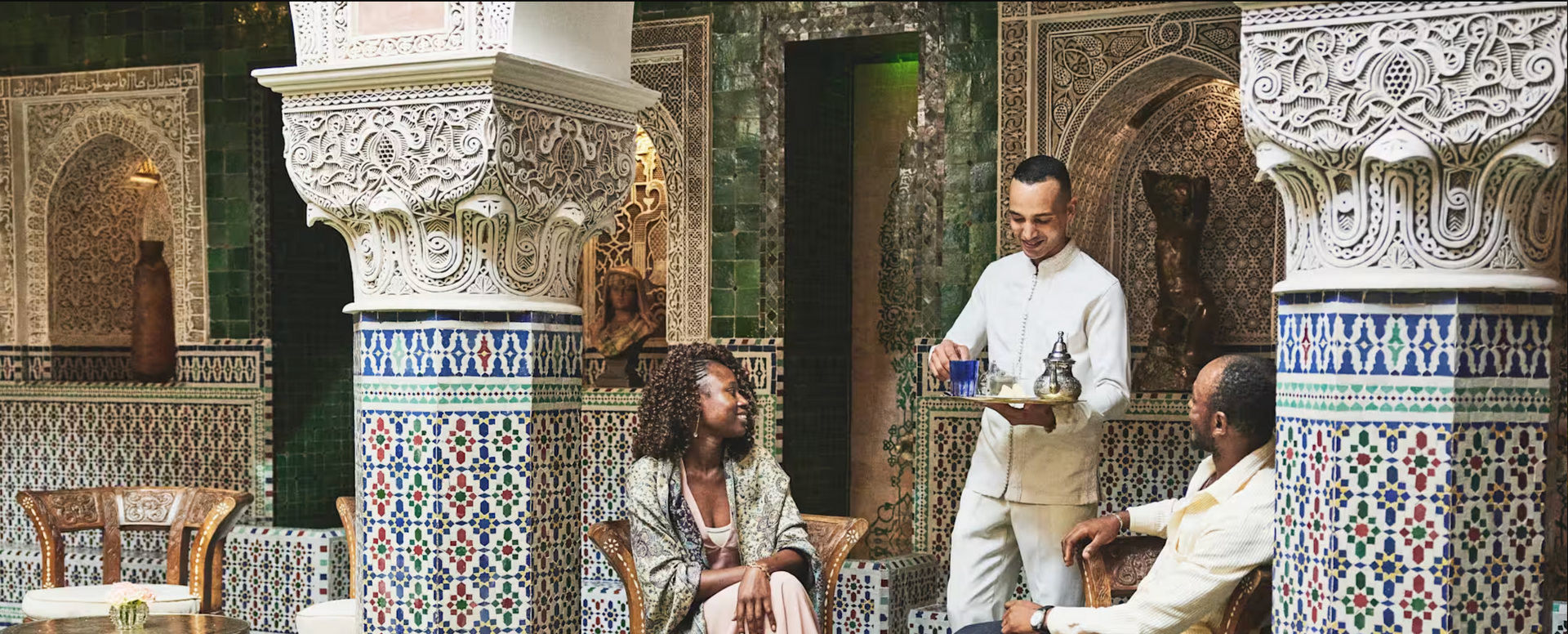A waiter serves tea to a couple in a decorated Moroccan-style room.