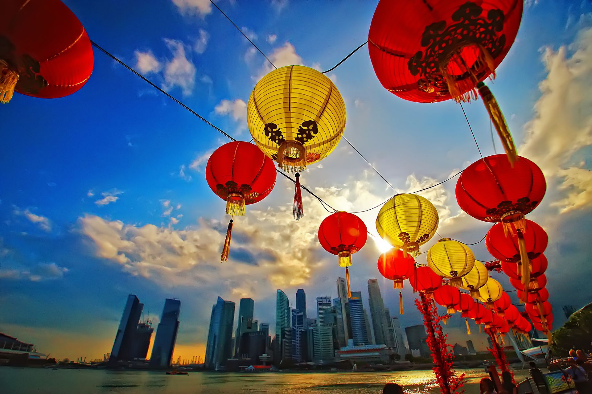 Red and yellow lanterns strung over Singapore skyline at sunset.