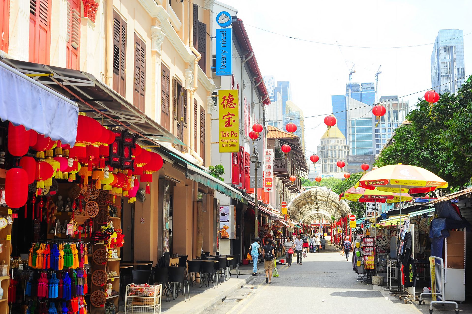 Street scene in Chinatown, Singapore, with shops, red lanterns, and buildings. People walk on the street.
