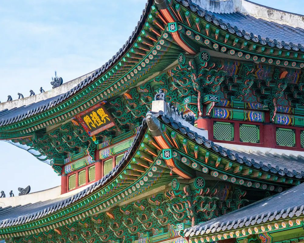 Ornate teal, red, and gold Korean palace roof against a blue sky.