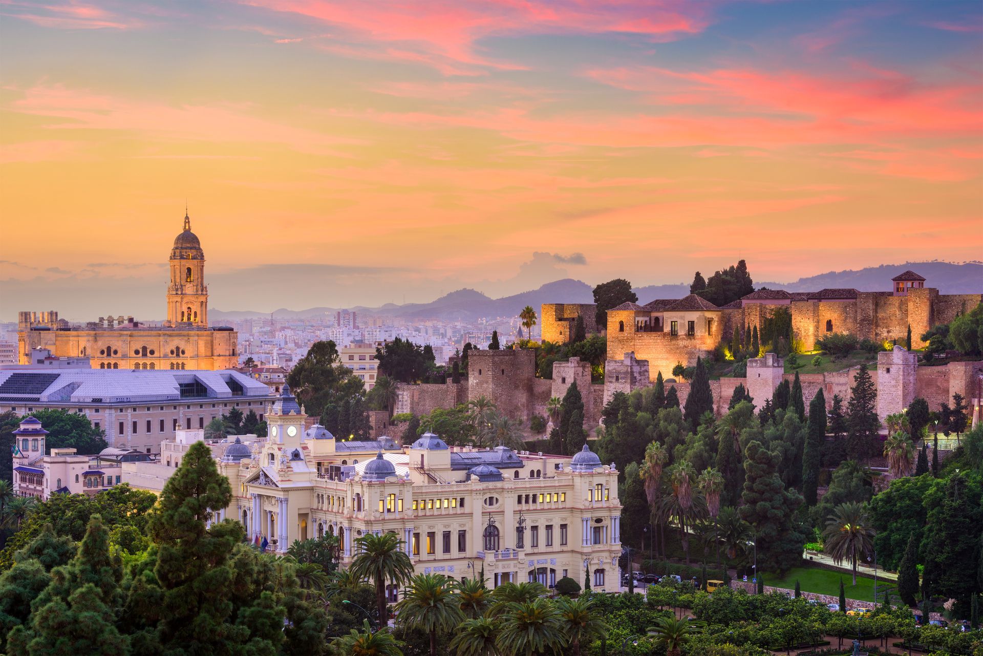 Cityscape at sunset: Malaga, Spain, with cathedral, Alcazaba fortress, and colorful sky.