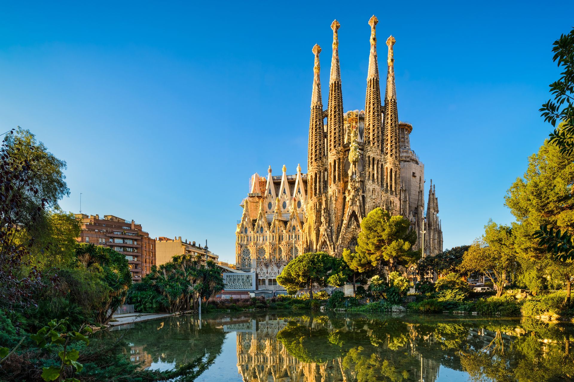 Sagrada Familia church reflected in a pond, Barcelona, Spain, under a clear blue sky.