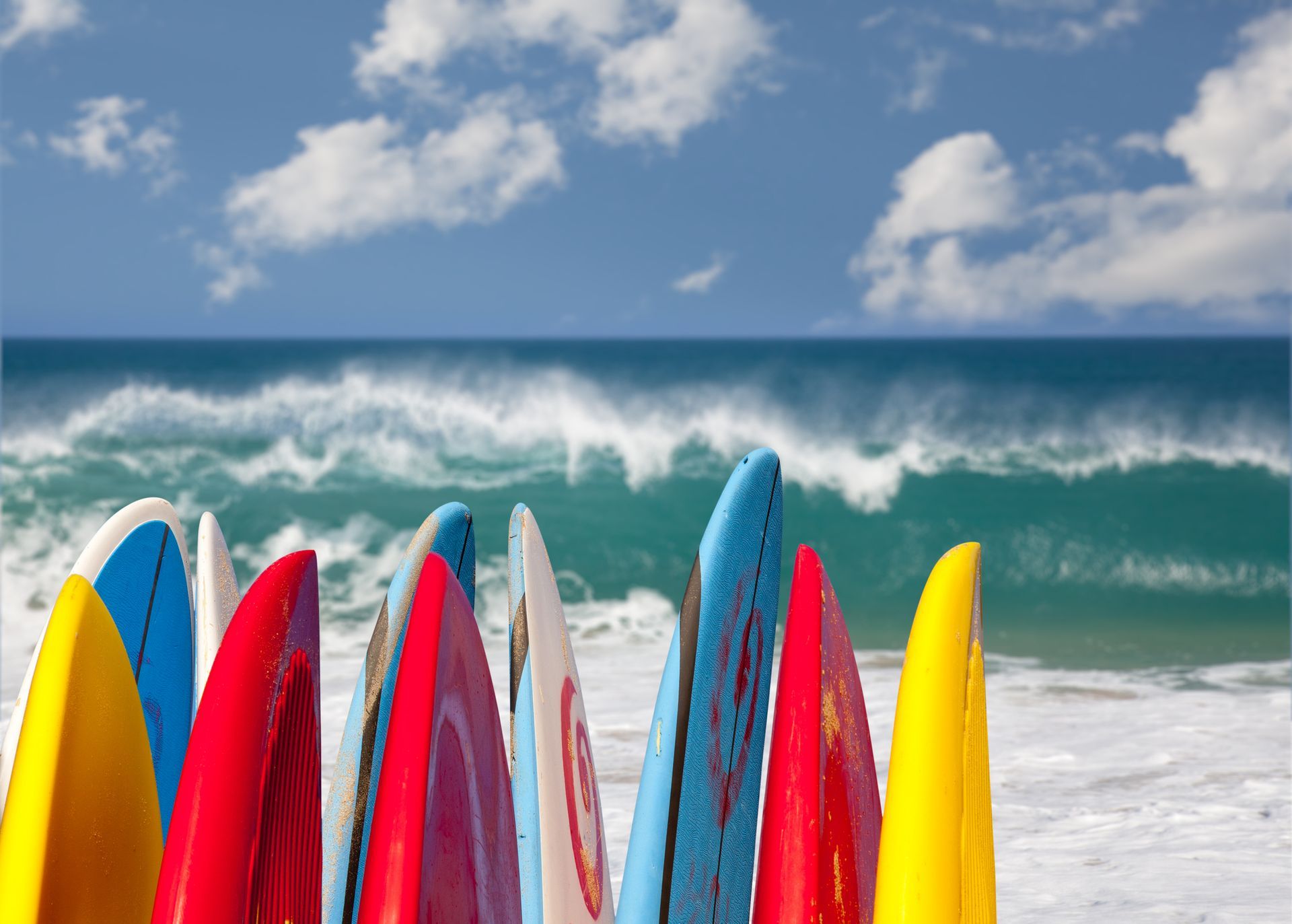 Colorful surfboards on a beach with ocean waves and a blue sky.