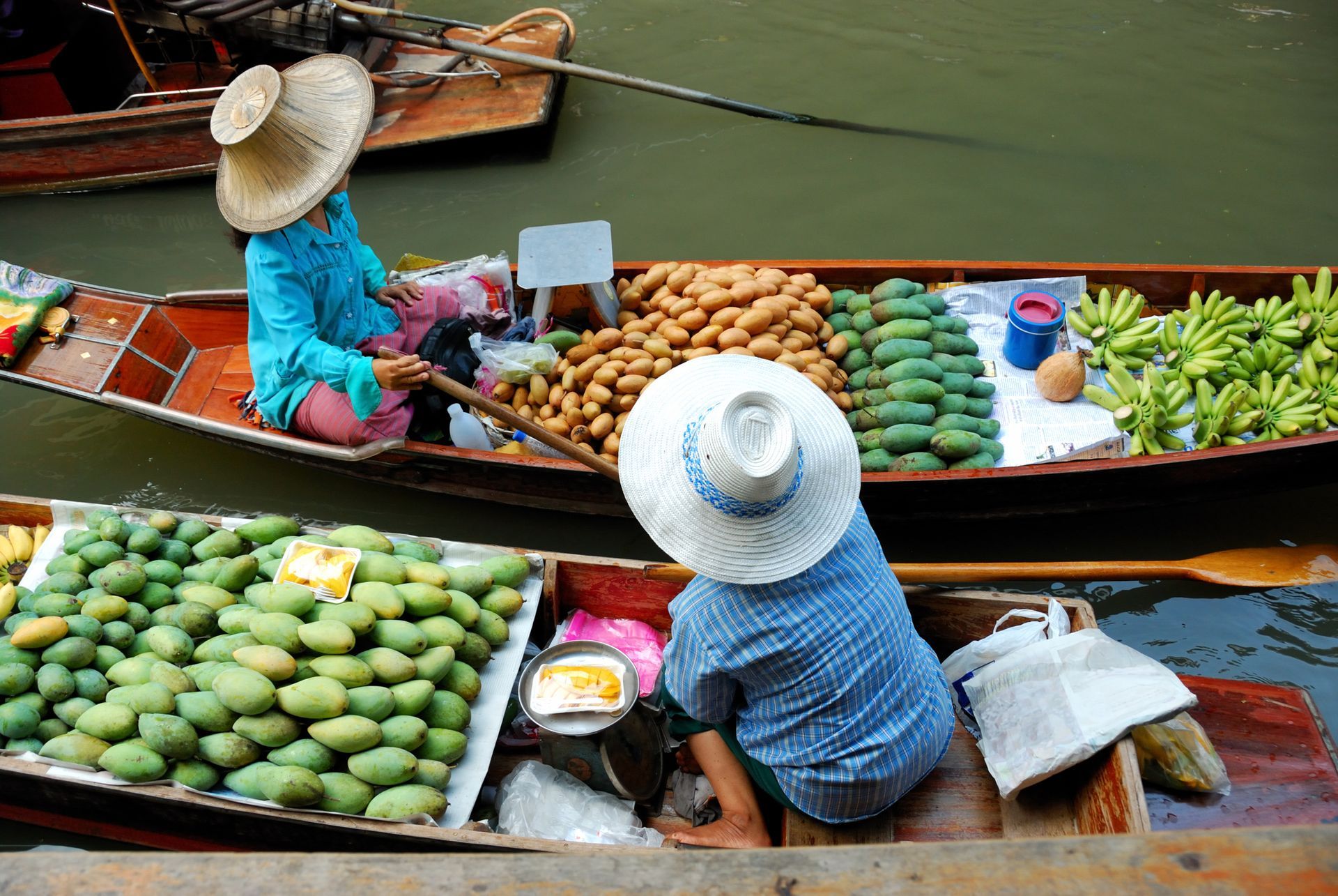 Boats laden with fruit at a floating market; two vendors in straw hats.