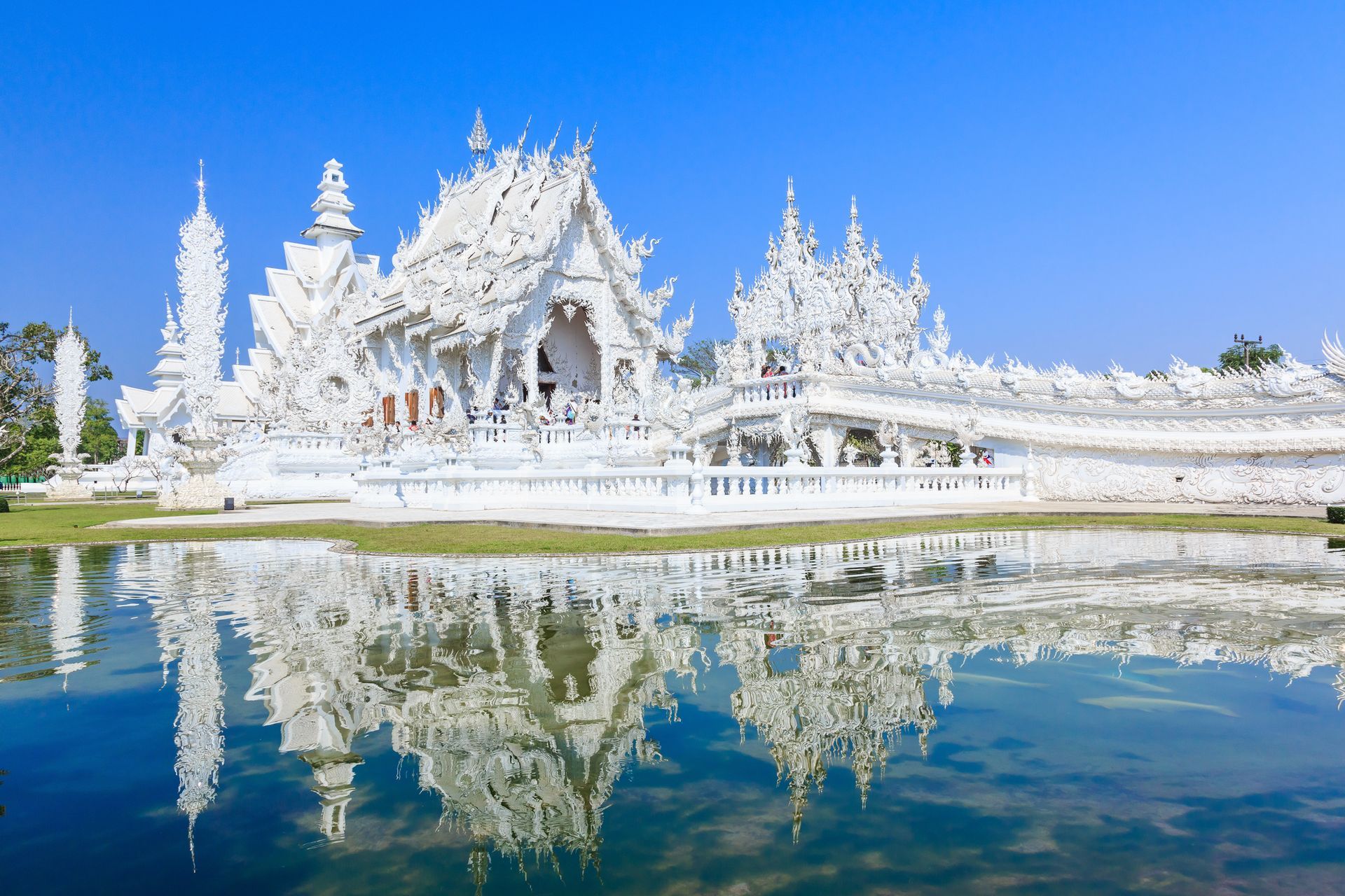 White temple complex reflected in water under a clear blue sky.