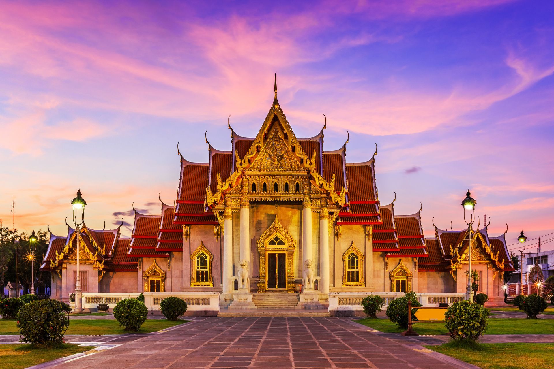 Temple with ornate gold roof and white columns, under a colorful sunset sky.