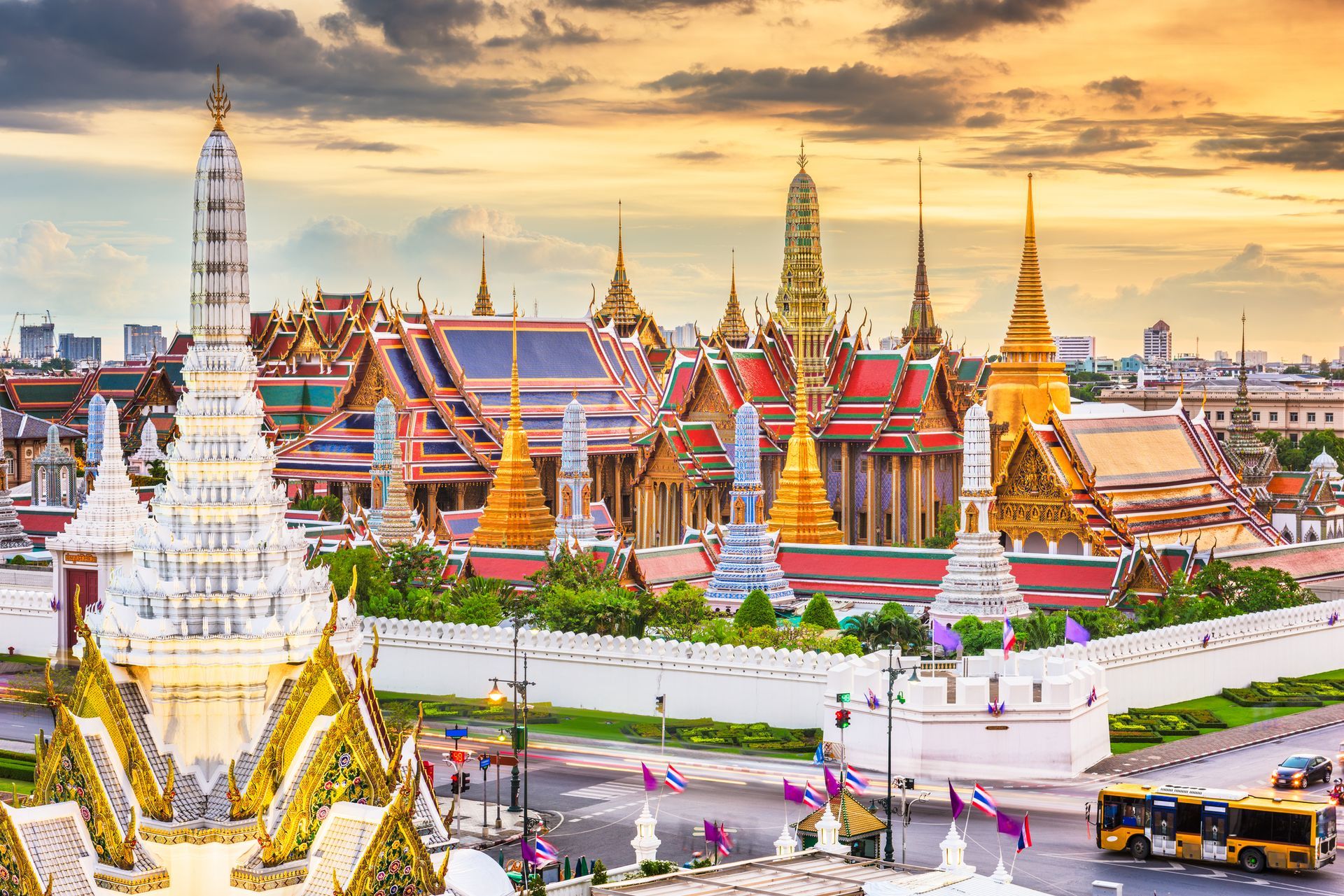 Golden spires and ornate buildings of the Grand Palace, Bangkok, Thailand, under a warm sunset sky.
