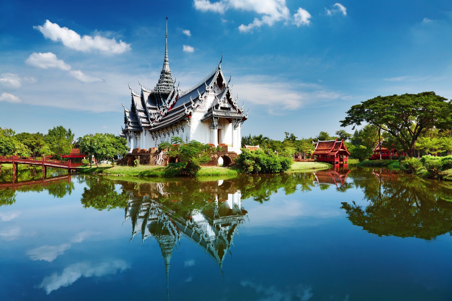 White temple with ornate roof reflected in still, blue water under a partly cloudy sky.