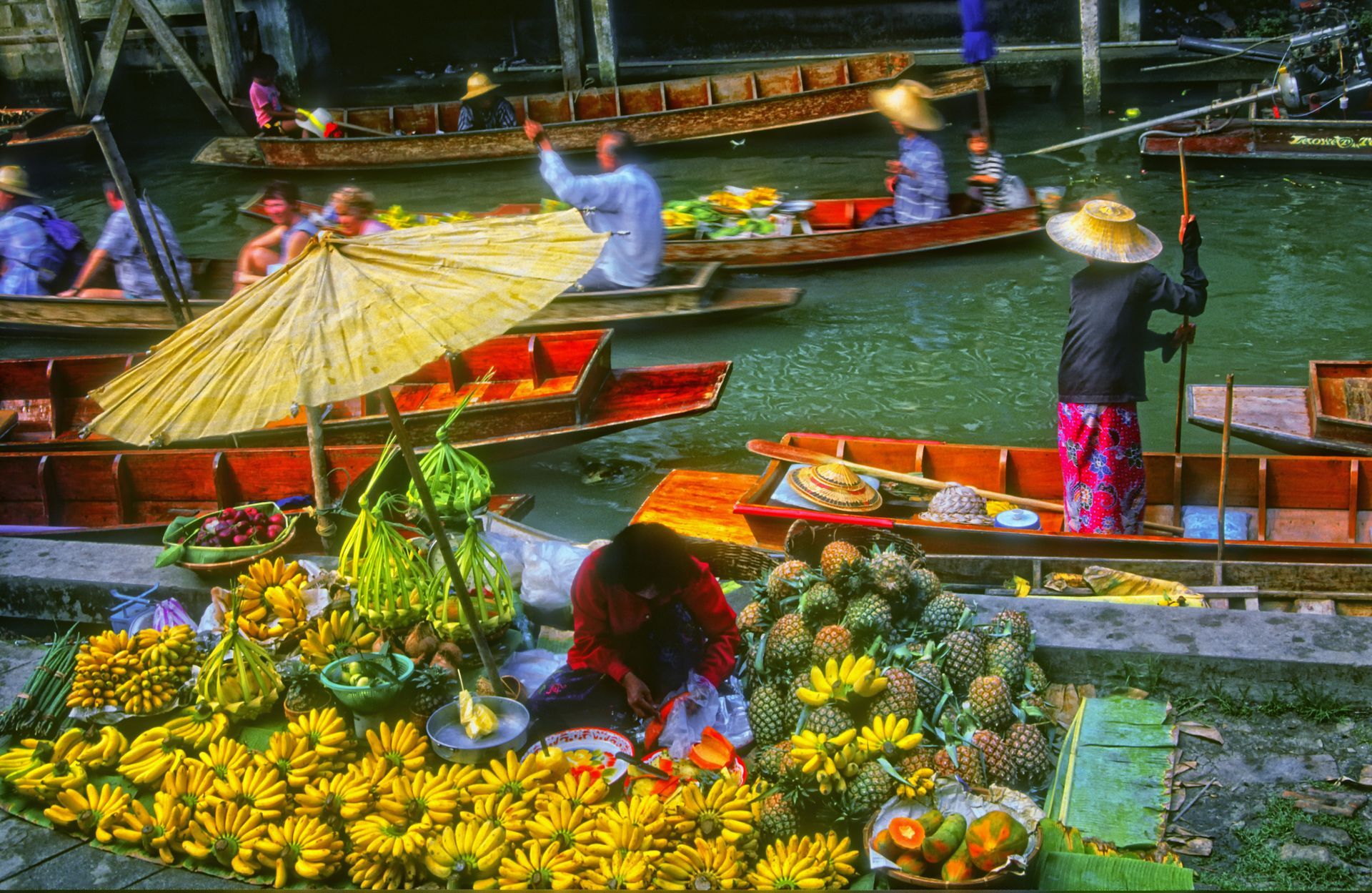 Floating market in Thailand, boats laden with produce, vendors, umbrella, canal water.