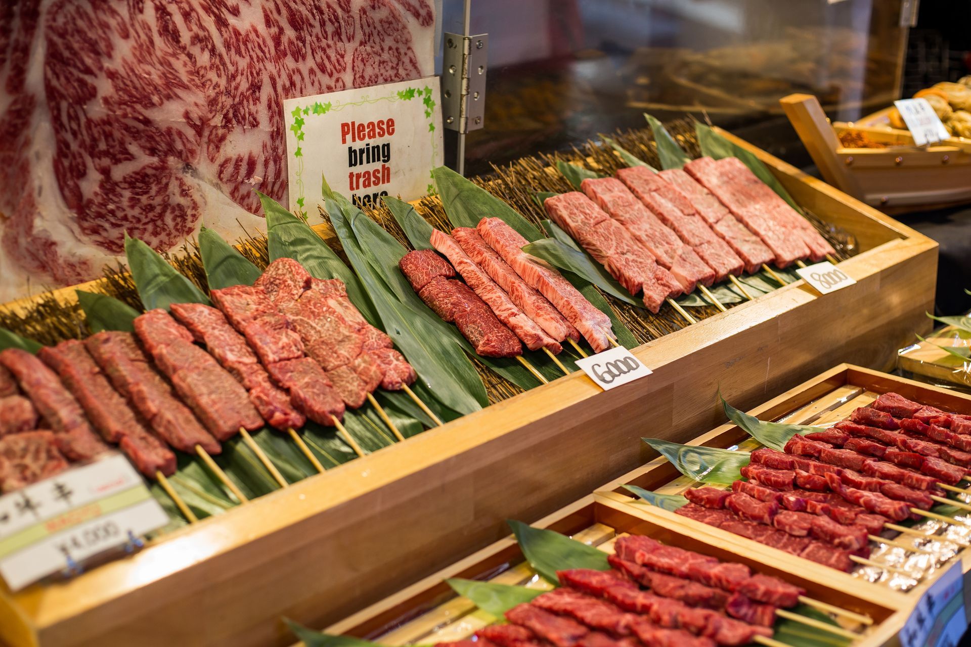 Display of raw, skewered beef at a food stall. Wooden trays hold various cuts arranged on green leaves.
