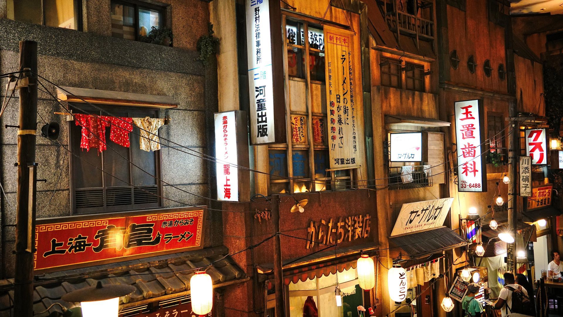 Night scene of Japanese street, with lit signs, lanterns, and shops.