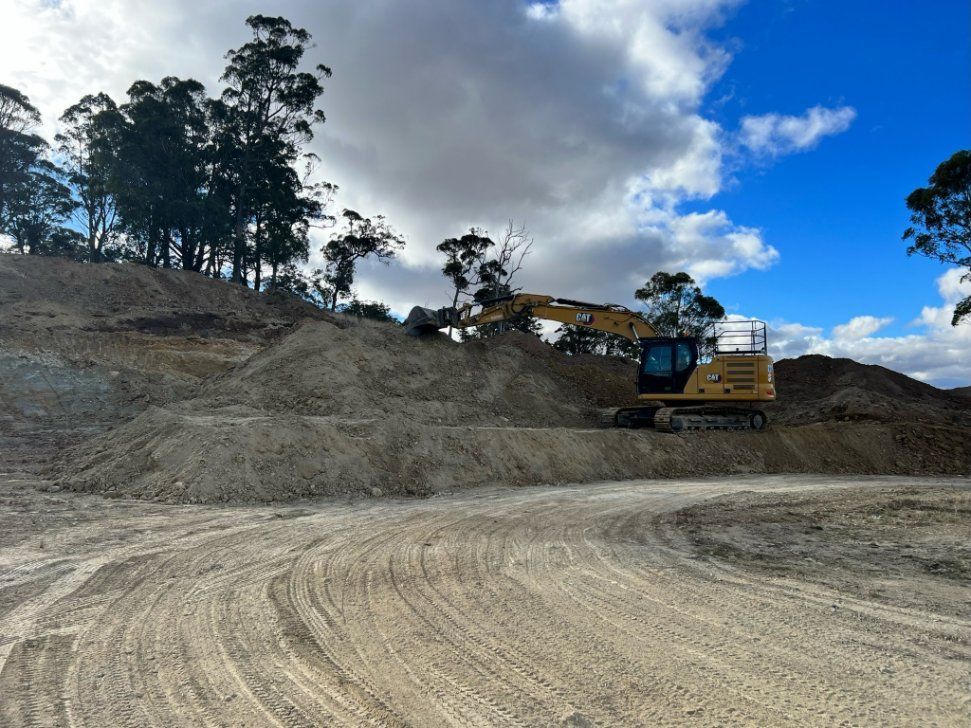 A Yellow Excavator Is Driving Down a Dirt Road — RC Civil in Armidale, NSW