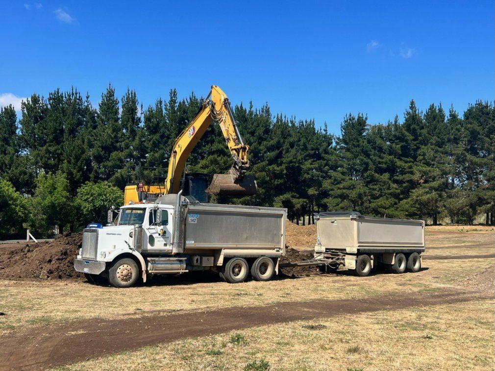 A Yellow Excavator Is Loading Dirt Into a Dump Truck — RC Civil in Armidale, NSW