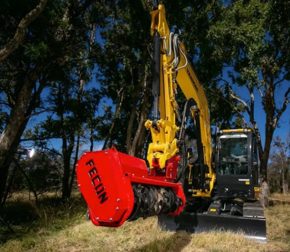 Yellow excavator equipped with a red Fecon mulcher attachment performing land clearing in a forested