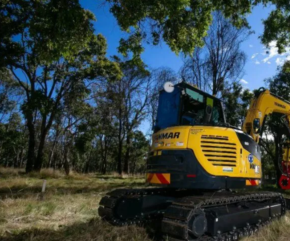 Yellow and red excavator under trees.