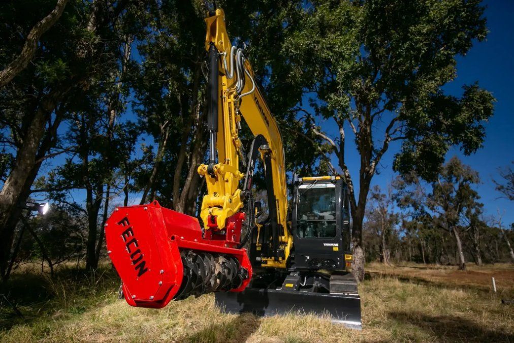 A Yellow Excavator Is Driving Through a Field with Trees in The Background — RC Civil in Armidale, NSW