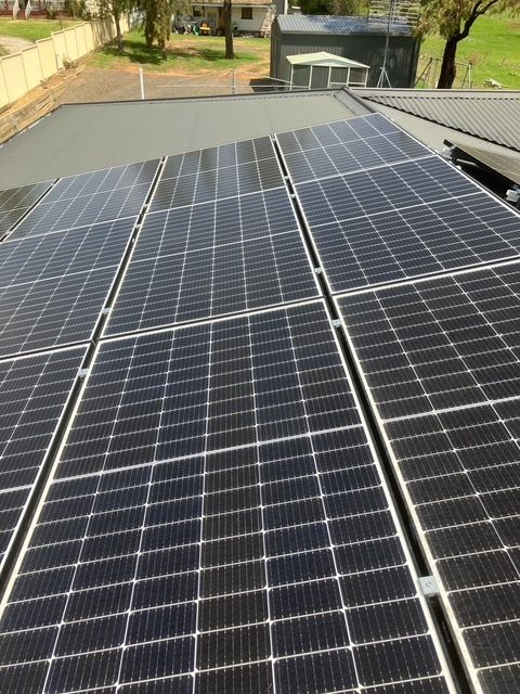 Solar panels installed on a black roof, with a residential setting in the background.  — Todd Basham Electrical in Temora, NSW