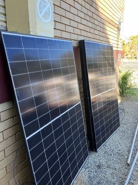 Two solar panels leaning against a brick wall, reflecting the sky. — Todd Basham Electrical in Cootamundra, NSW