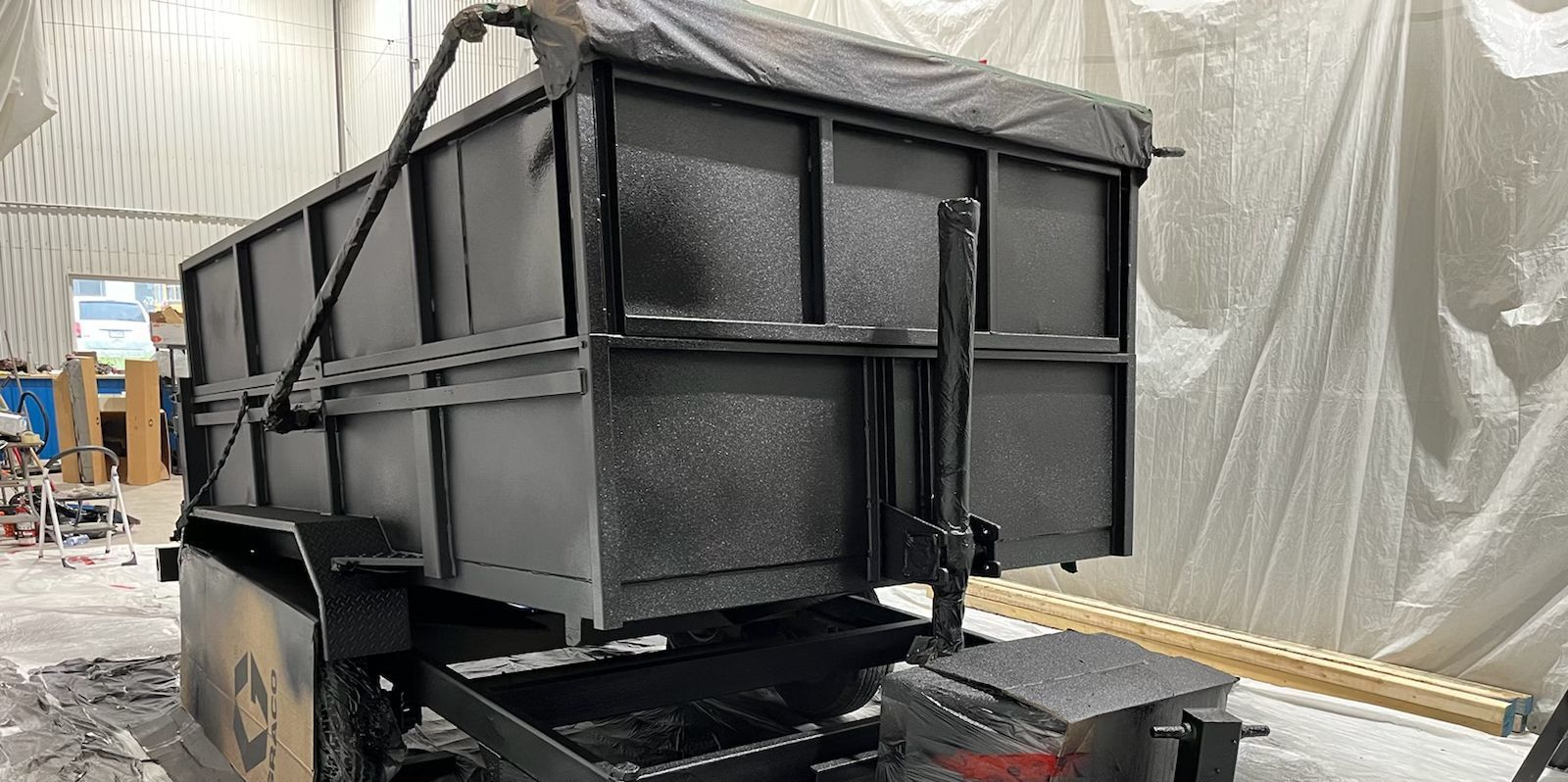 Une remorque à benne noire dans un atelier, recouverte d'une bâche.