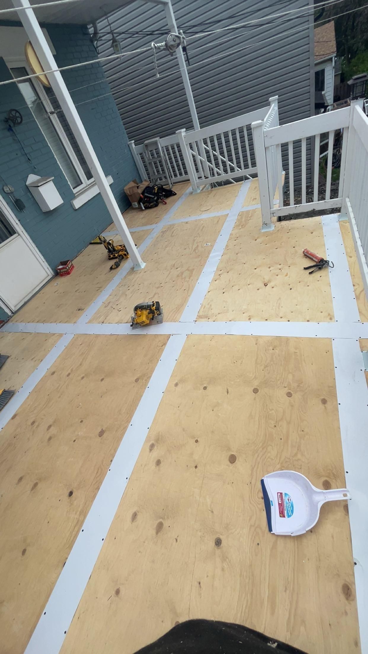 Terrasse en construction avec outils et garde-corps blanc. Bois clair, contreplaqué, mur bleu.