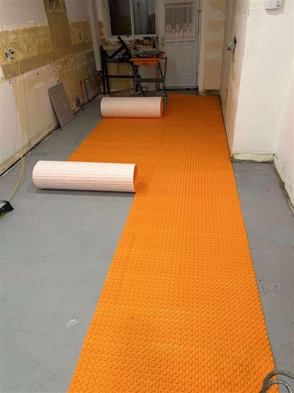 Rouleaux de sous-couche orange sur un sol en béton gris dans une pièce, préparé pour l'installation du revêtement de sol.