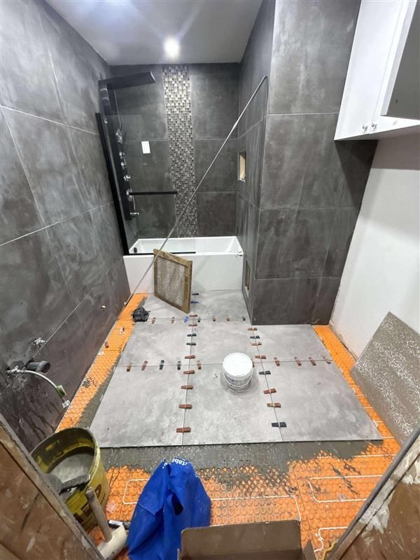 Salle de bain en construction avec murs et sol carrelés gris, baignoire et outils de carrelage.