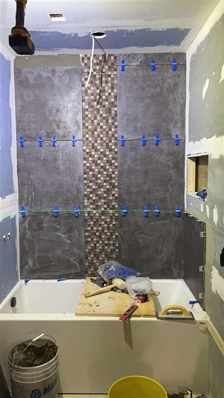 Rénovation de salle de bain en cours, comprenant des murs carrelés, une baignoire, des outils et un accent de mosaïque.