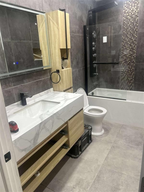 Salle de bain moderne avec vanité en bois clair, comptoir en marbre, toilettes et douche avec cadre noir.