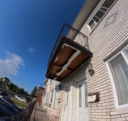 Immeuble en briques blanches avec balcon, ciel bleu, voitures garées.