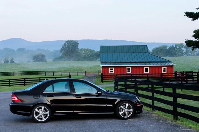 A black car is parked in front of a red barn