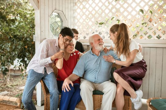 A family is sitting on a porch talking to each other.