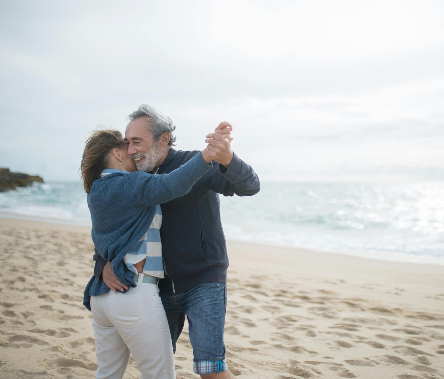 An elderly couple is dancing on the beach.