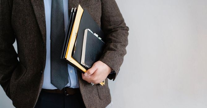 A man in a suit and tie is holding a stack of case files.