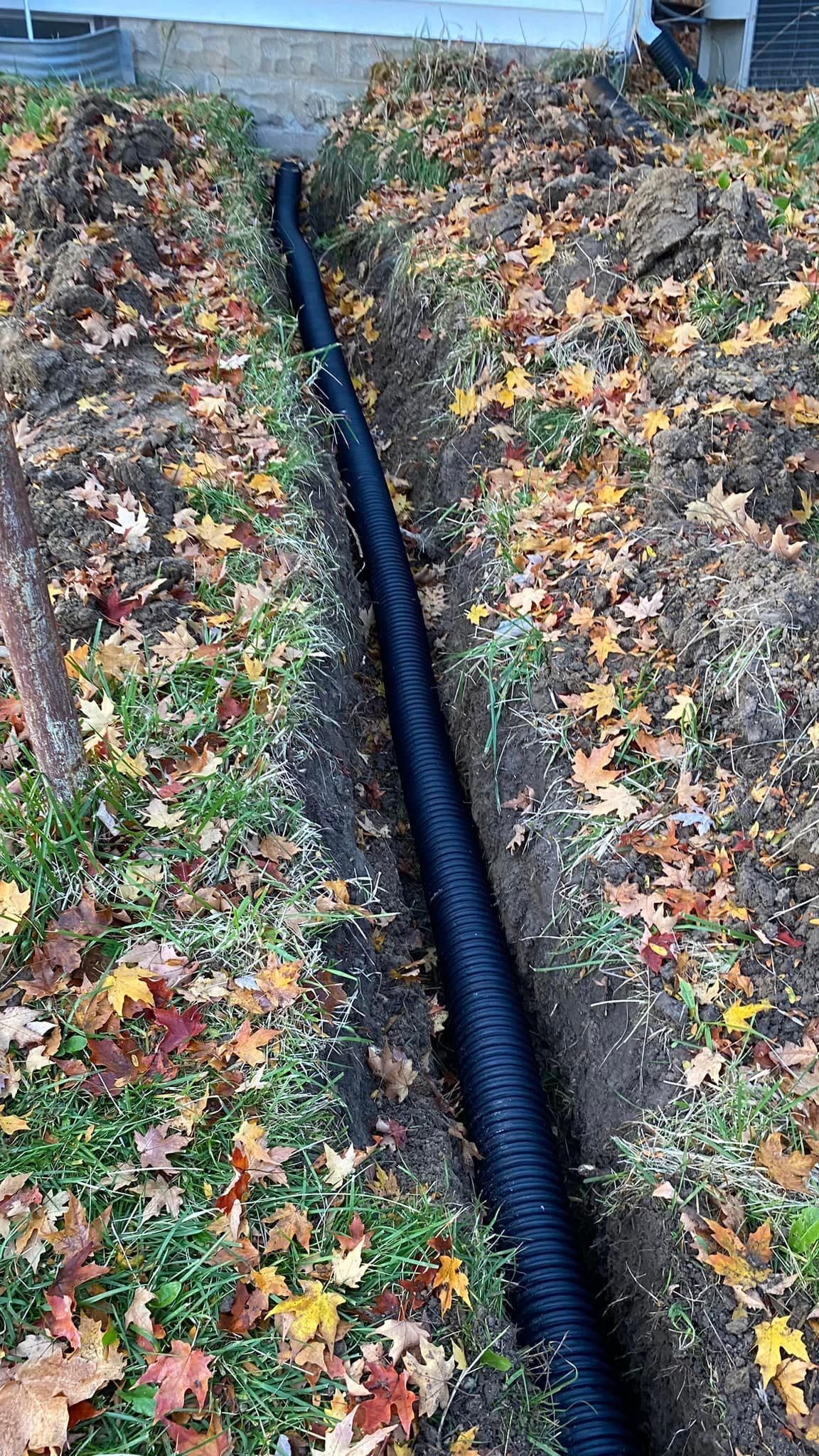 A black pipe is laying in the dirt next to a house.