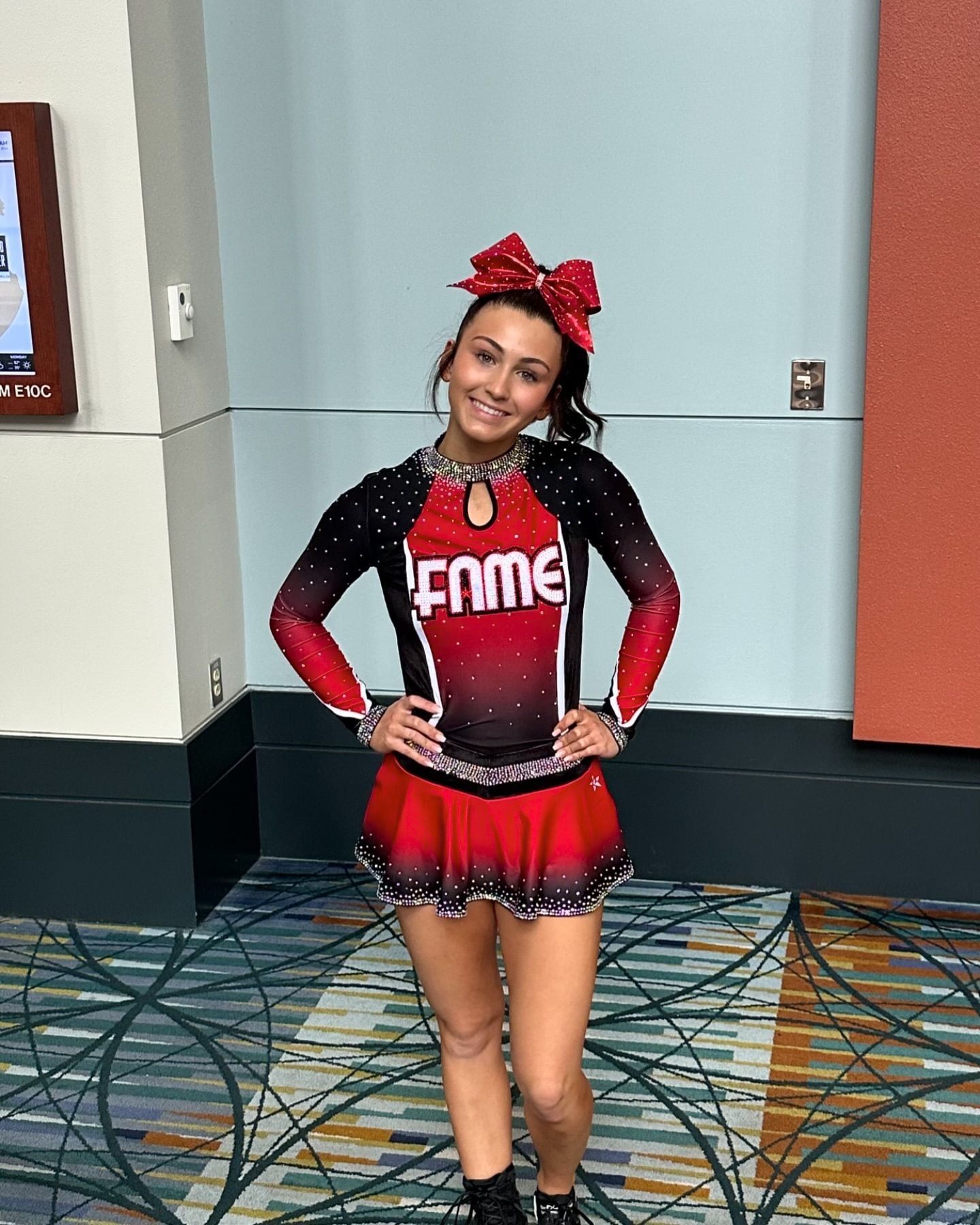 A cheerleader is standing in a hallway with her hands on her hips.