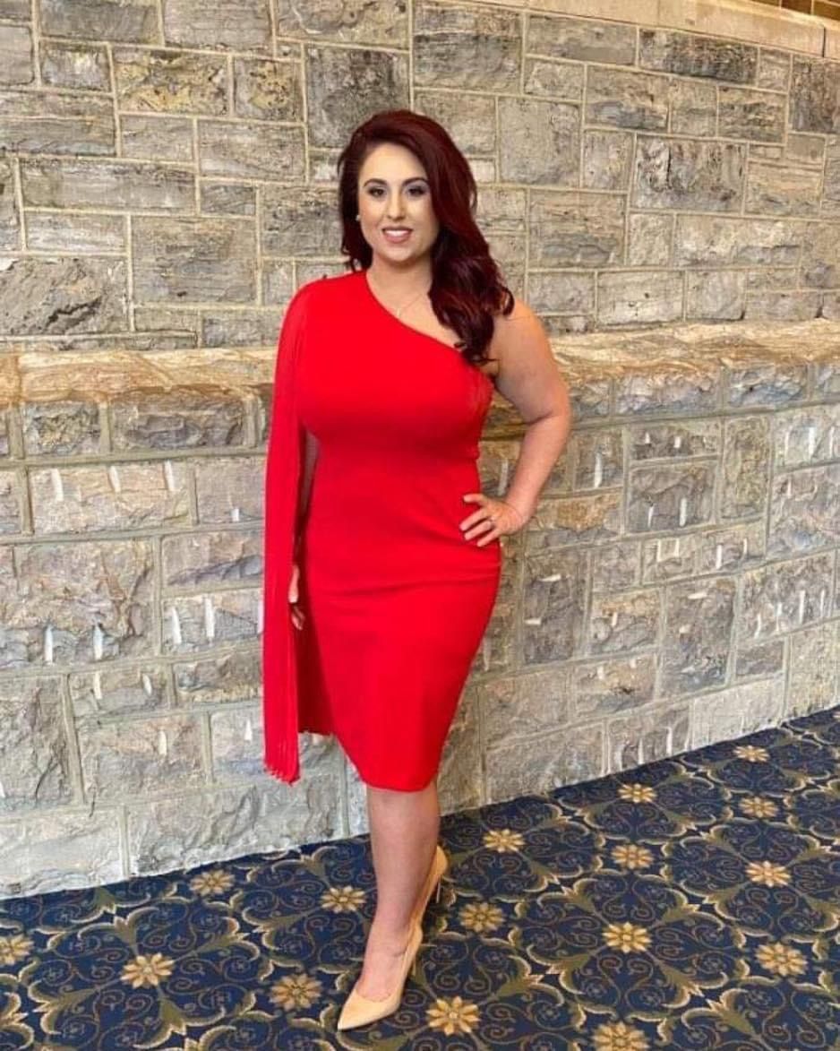 A woman in a red dress is standing in front of a brick wall.