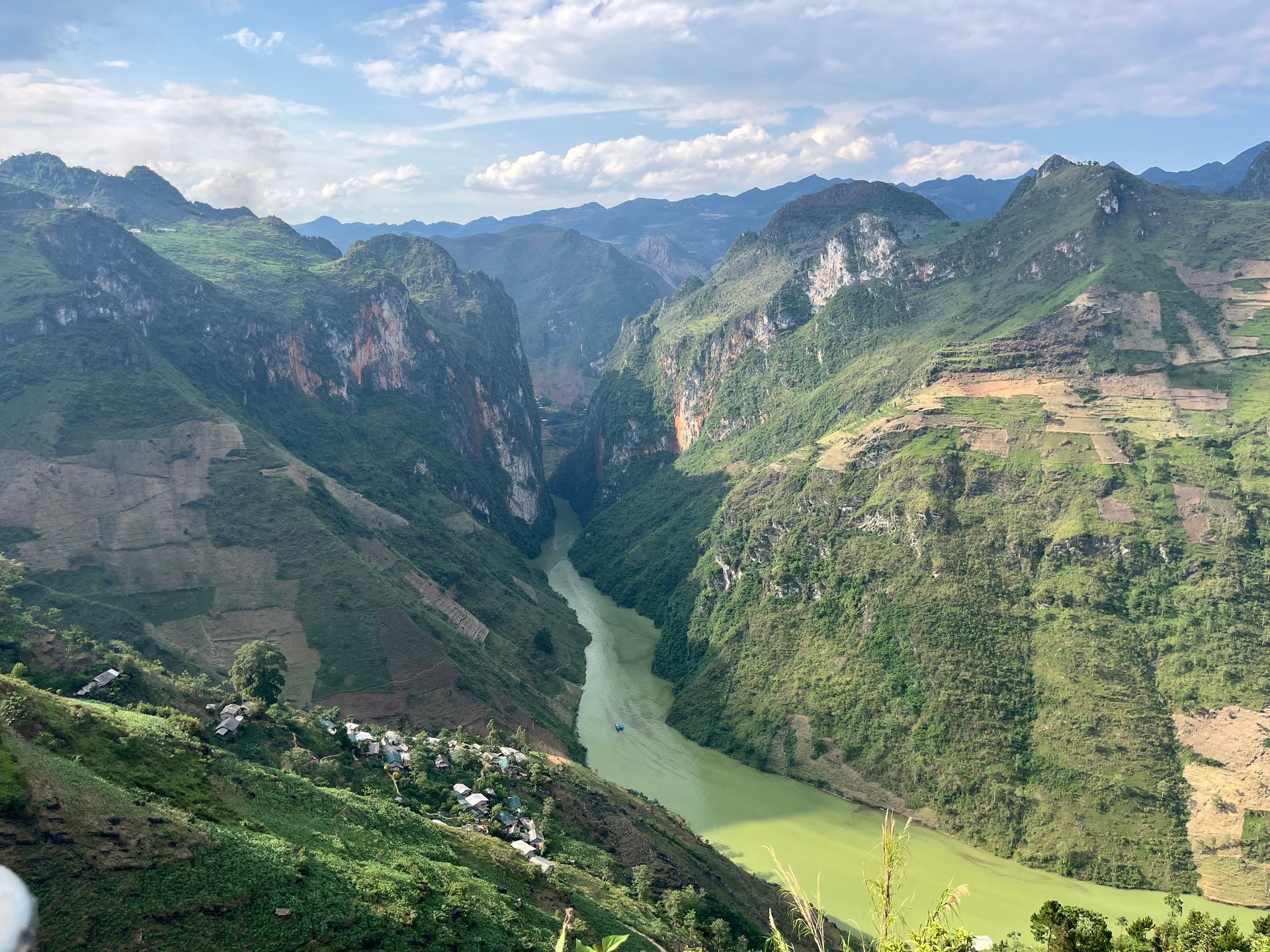 A lush green valley with a river winding through towering cliffs and mountains under a blue sky. Vietnam