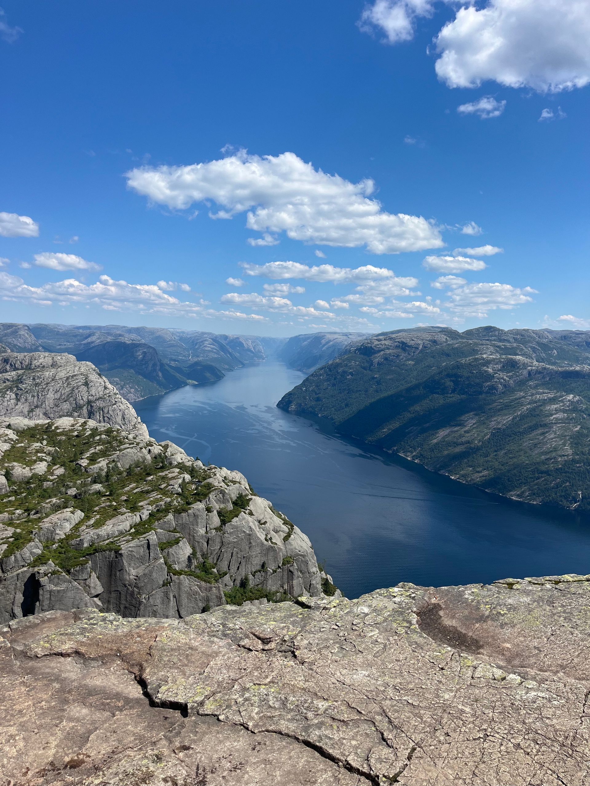 View of a blue fjord in Norway between rocky cliffs under a partly cloudy sky.