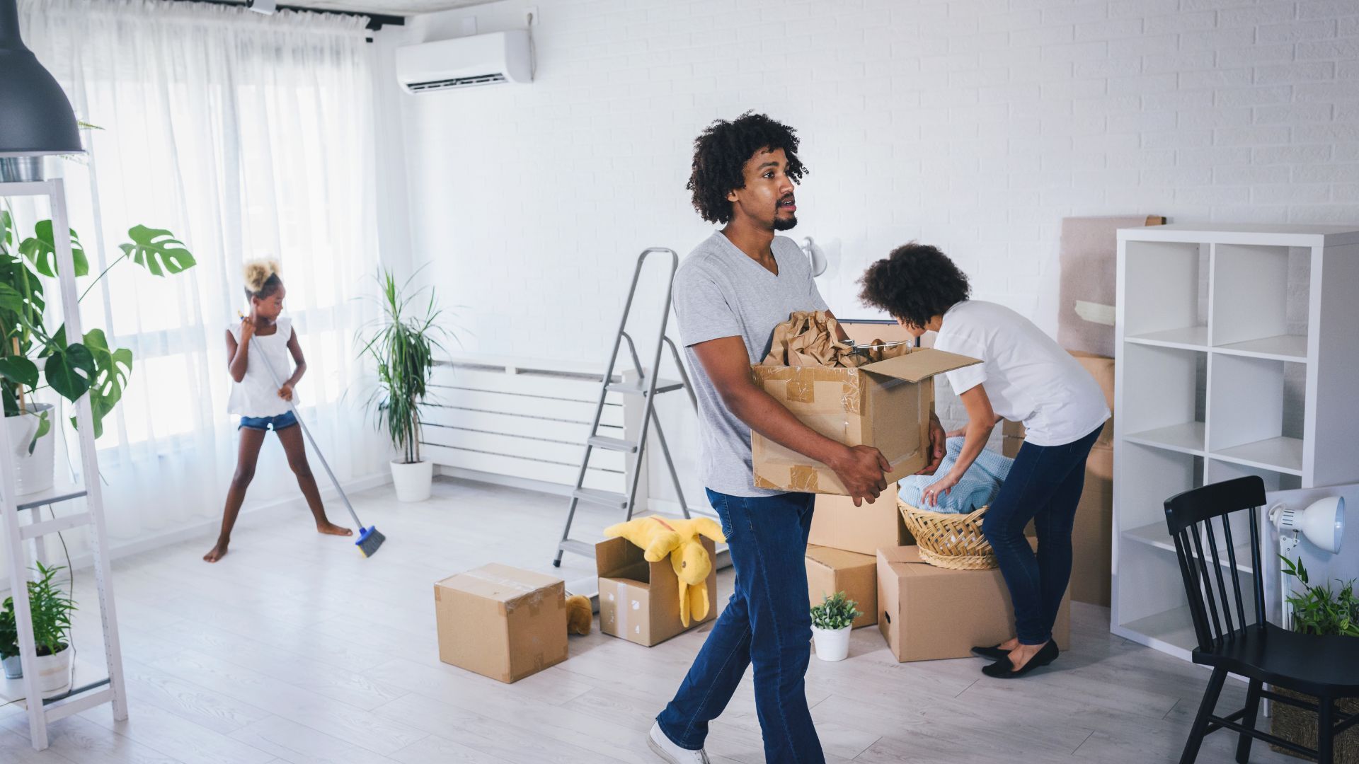 A man and woman are carrying boxes in a living room.