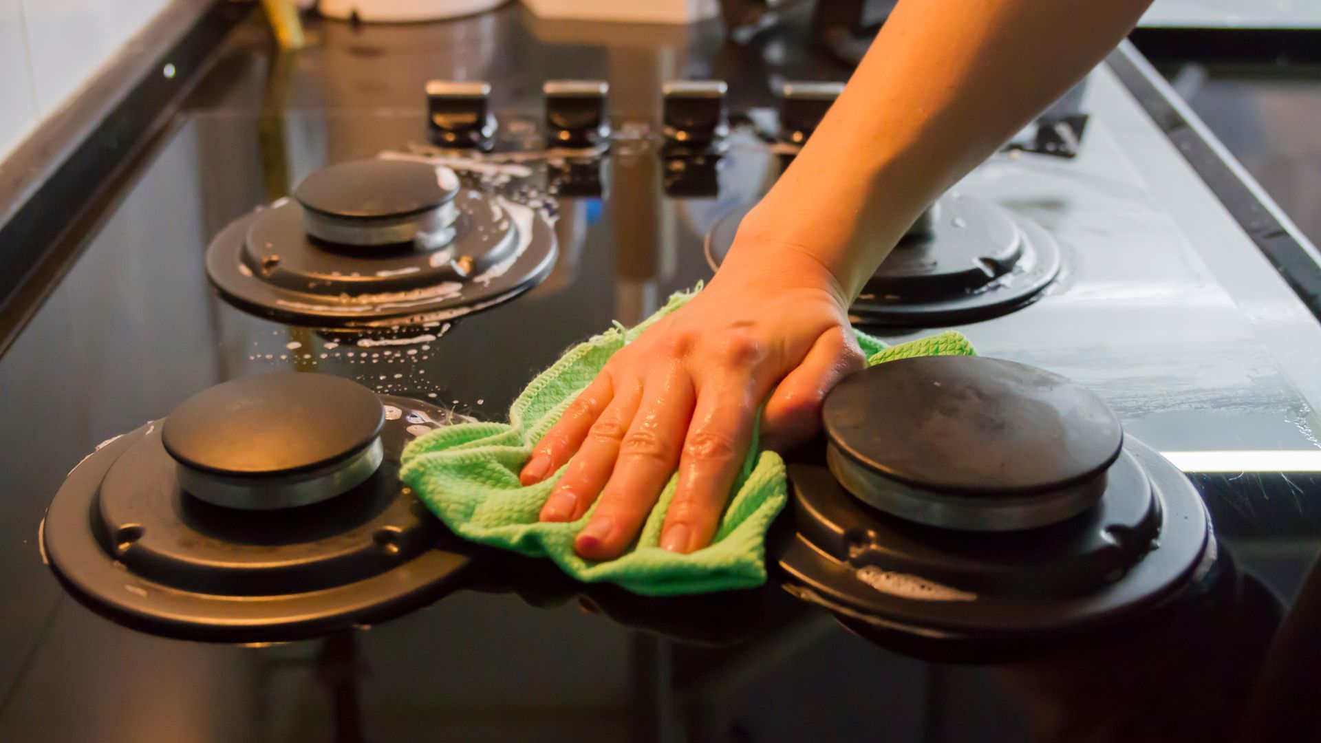 A person is cleaning a stove top with a cloth.