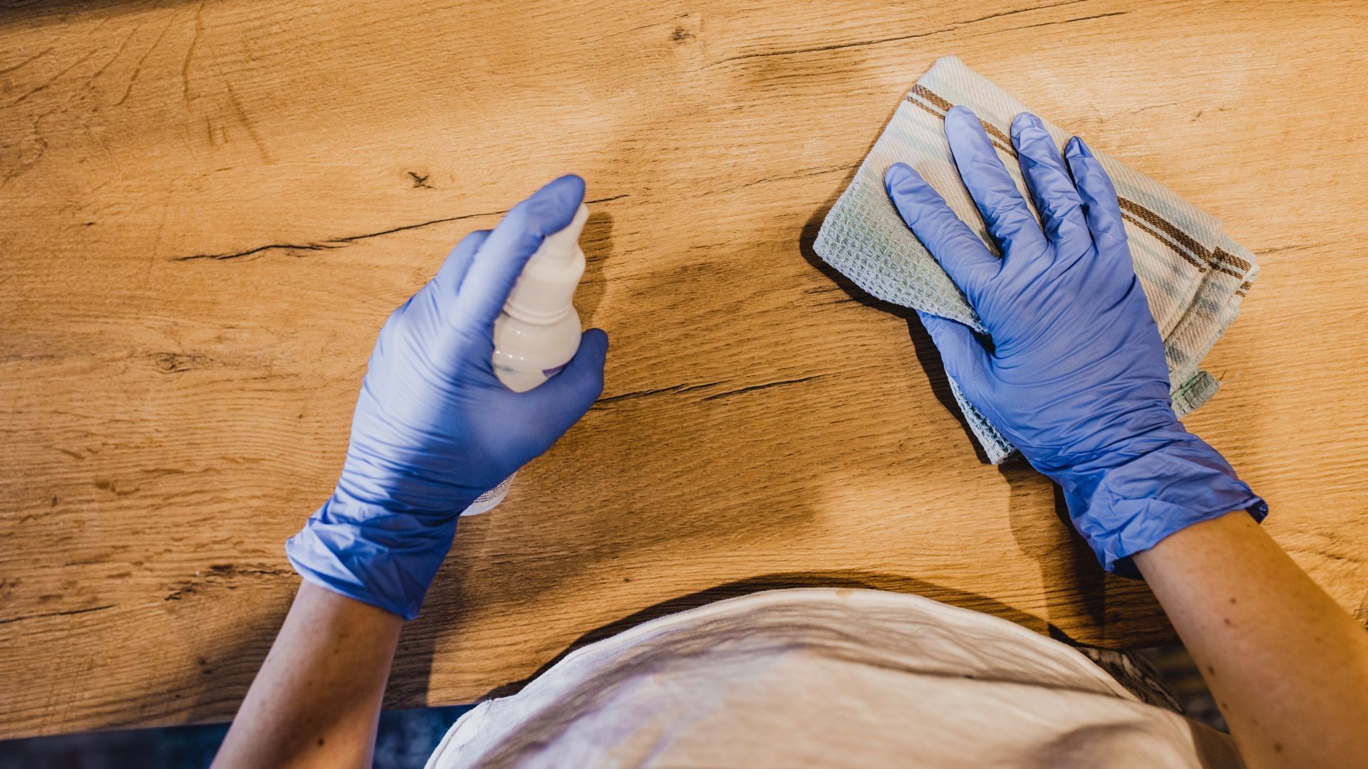 A person wearing blue gloves is cleaning a wooden table with a cloth.