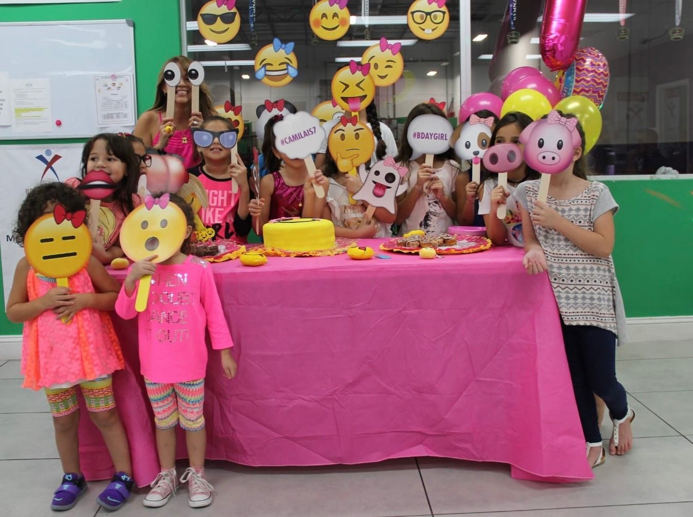 Un grupo de chicas jóvenes están de pie alrededor de una mesa sosteniendo máscaras de emoji.
